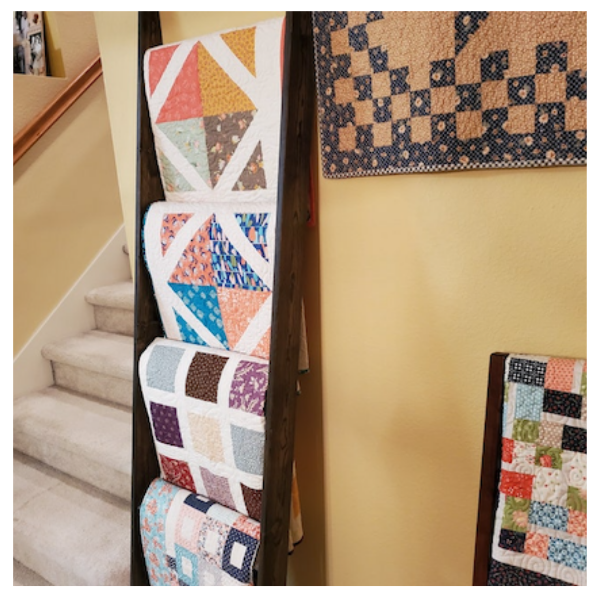 6 foot dark walnut stained blanket ladder. Four quilts are hung all with unique colorful patchwork.